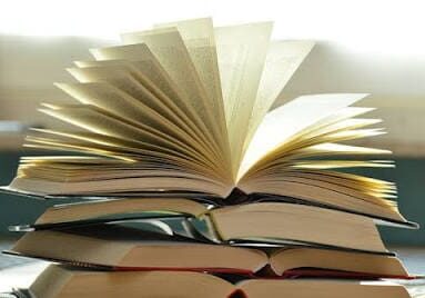 A stack of books with one open, pages fanning out.